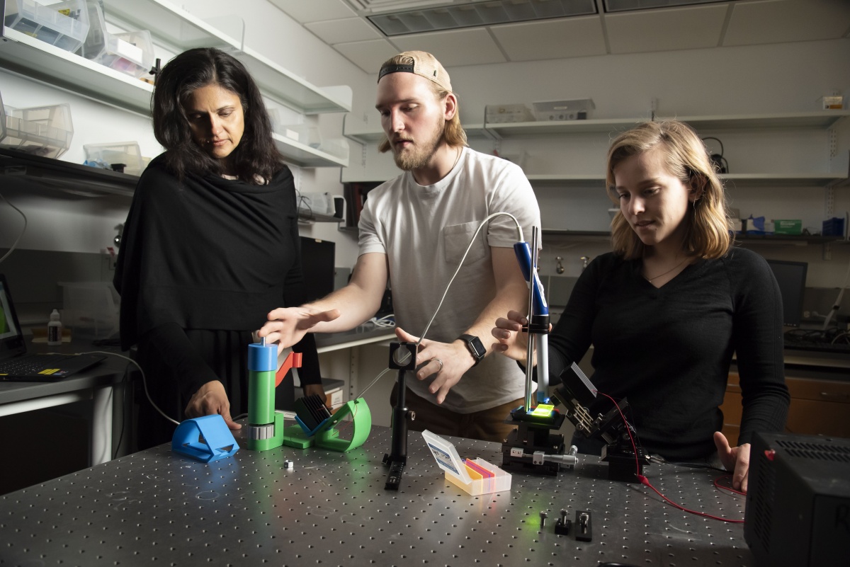 Graduate students Riley Deutsch (center) and Corrine Nief (right) use a scope in the lab with Ramanujam's guidance. 