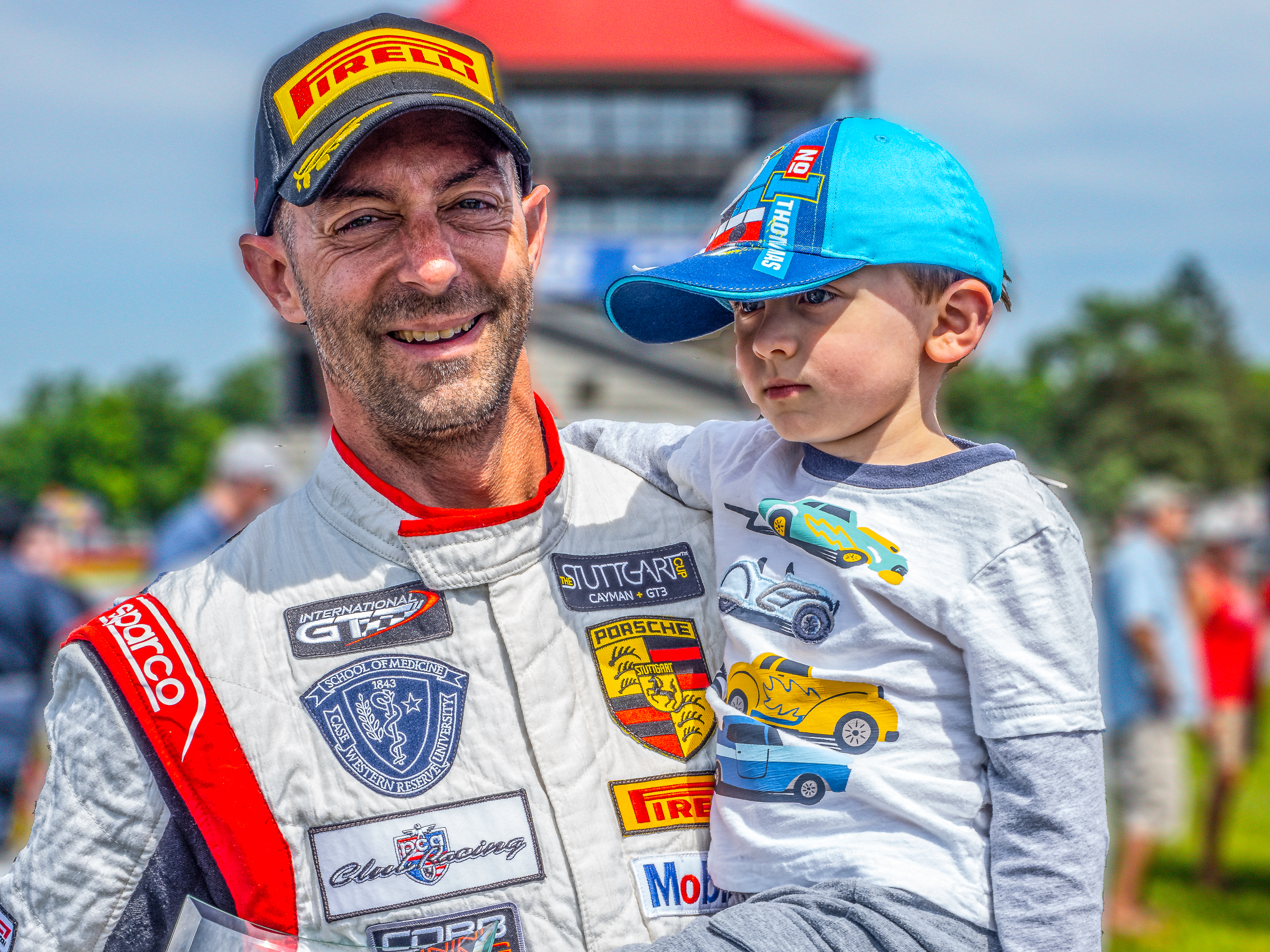 A man holding a young child in a racing suit at a speedway