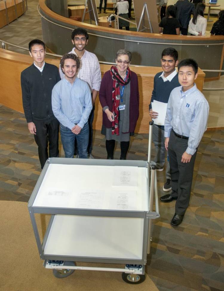 A team of first-year engineers stand around their prototype book cart