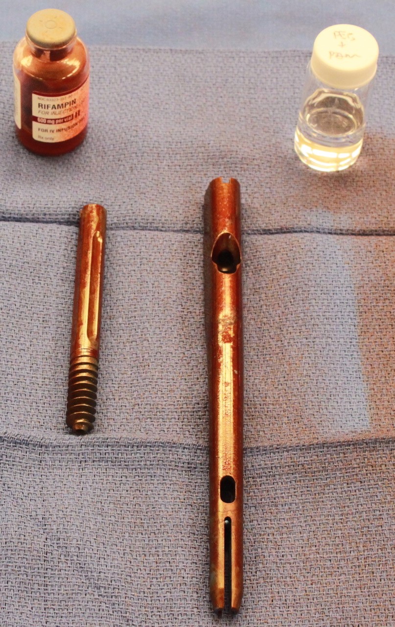 Two long devices coated with a copper colored substance and two small bottles sitting nearby