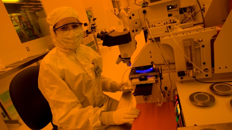female student in clean room suit at microscope