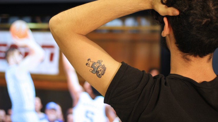 man's arm with UNC mascot tattoo and basketball game in the background