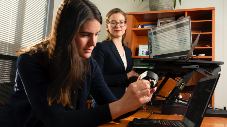 Ph.D. student Brinnae Bent prepares to download information from a wearable health monitoring device while assistant professor Jessilyn Dunn looks on. (Les Todd) 