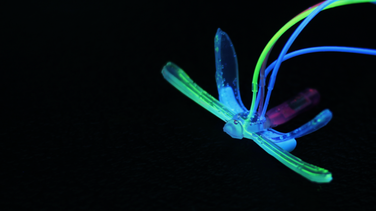 A dragonfly-shaped robot lit up in neon colors on a black background
