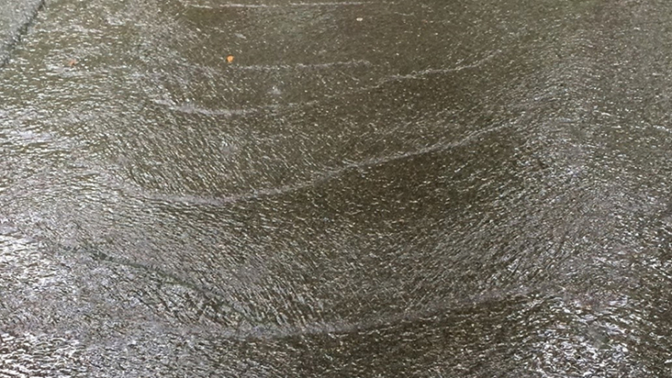 A sheet of water with ripples running over a concrete driveway