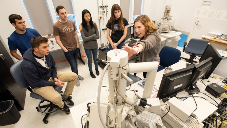 A group of students watch a researcher explain a large technical piece of equipment