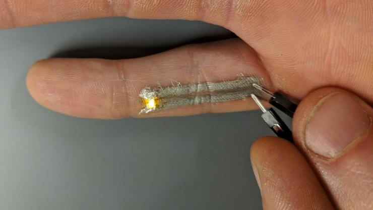 A pinky with two gray lines on the underside with an electrode at one end and a lit-up LED at the other
