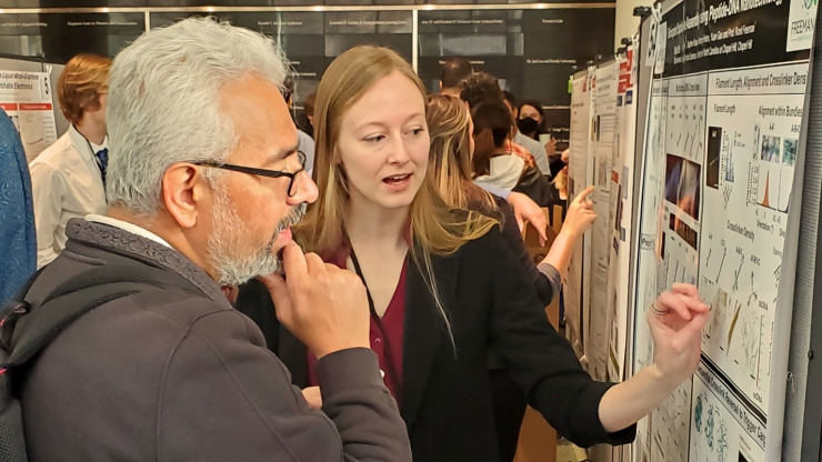 man and woman at conference discussing research while woman points at poster