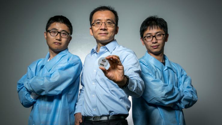 Tony Jun Huang holds out a tiny prototype device while flanked by two graduate students