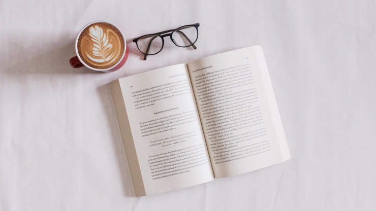 Open book with reading glasses and cup of coffee