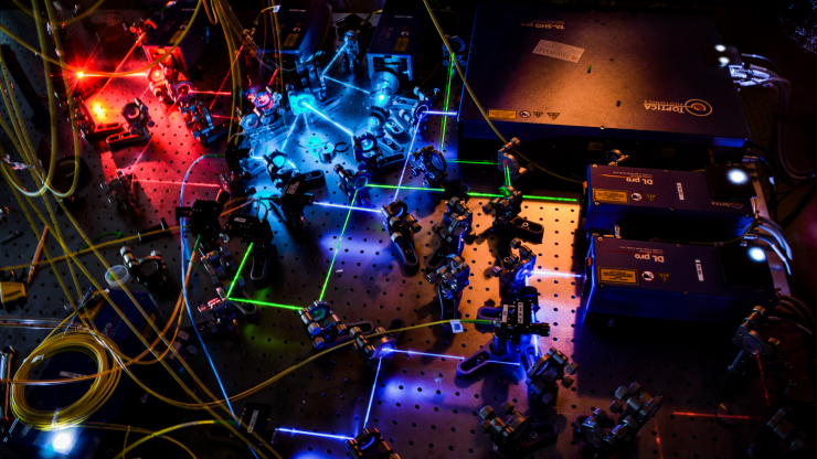 A bunch of machines lit with blue and red light with a maze of lasers running between them