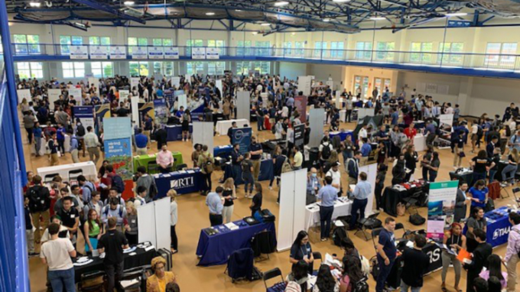 People crowd a gymnasium full of tables and stands