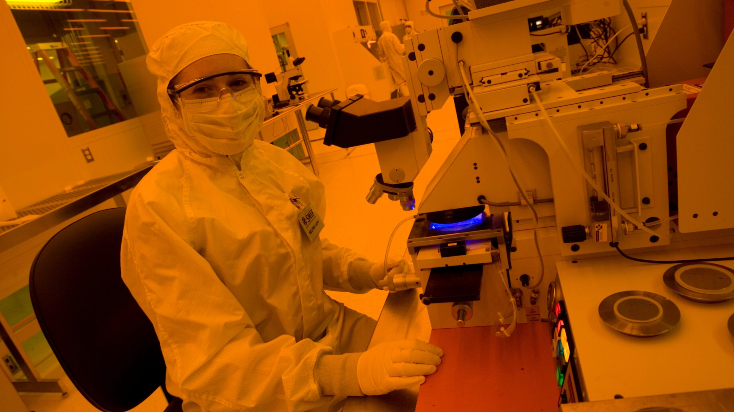 female student in clean room suit at microscope