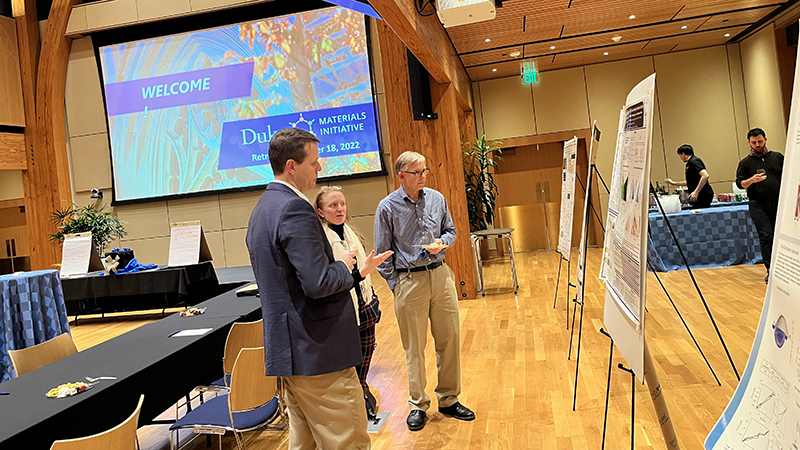 Three people stand by a research poster in a giant wood-laden room