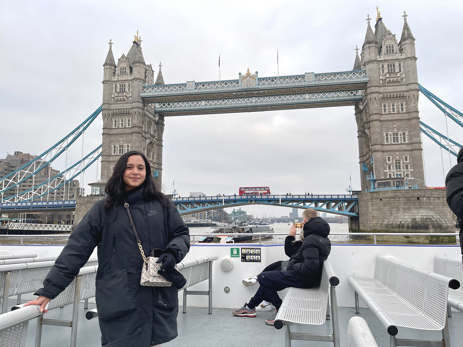 A woman stands on a sightseeing boat with old London bridges in the background