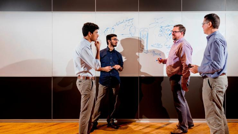 Four men standing at a white board with drawing on it