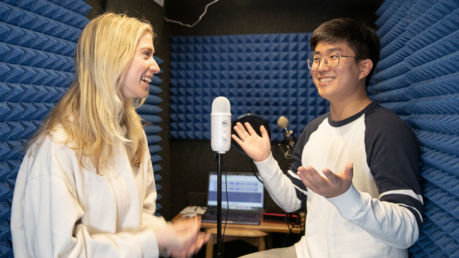 a male and female student laugh together in a sound recording booth