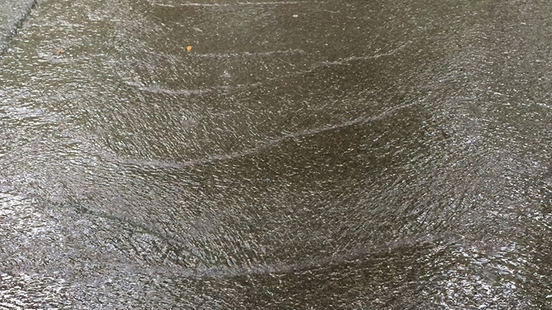 A sheet of water with ripples running over a concrete driveway