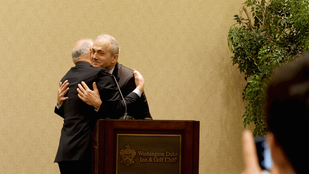 Two men hug and congratulate each other on a stage