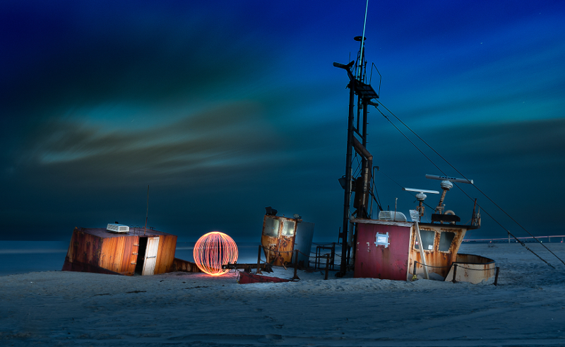 A small fishing boat on a beach at night illuminated by a glowing orb nearby