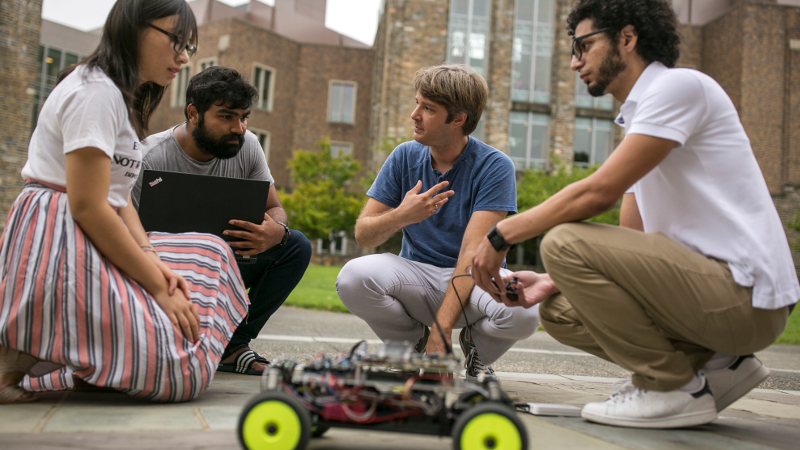 students and professor examine a four-wheeled autonomous vehicle