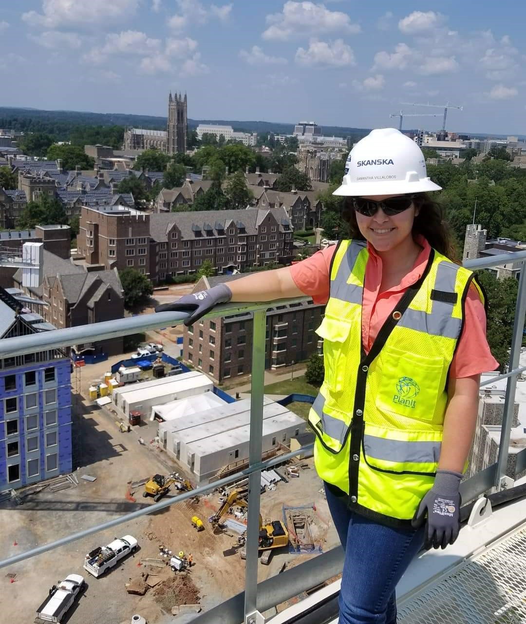 A woman in construction gear on a roof with a campus behind her