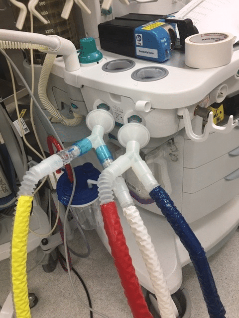 Two plastic ventilator splitters poking out of a machine, each with different colored tubes running out of them