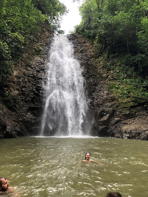 Students swim in a pool at the base of a waterfall in the jungle