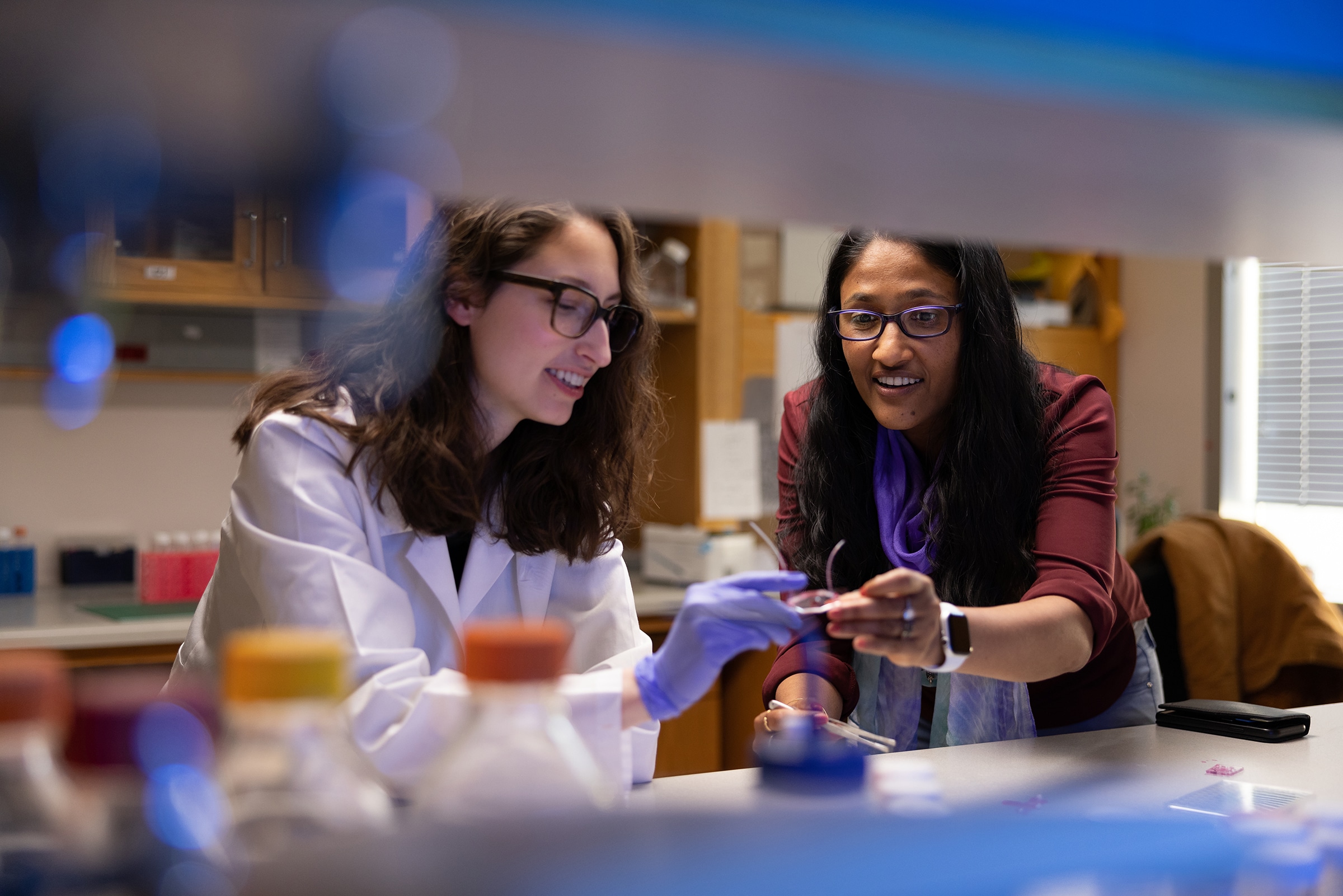 Shyni Varghese, professor of biomedical engineering, mechanical engineering and materials science and orthopaedics (right), in her Duke University lab. She is taking a microscope slide from a colleague.