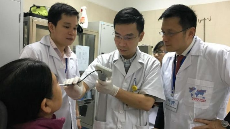 Three male doctors stand around a patient who is getting her throat scoped