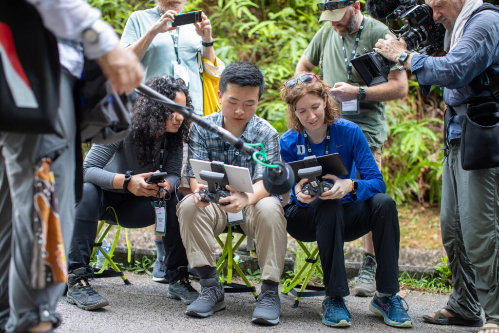Alexandra Rivera, Alex Xu and Juliet O’Riordan are
surrounded by a documentary film crew as they fly a
drone into the forest.