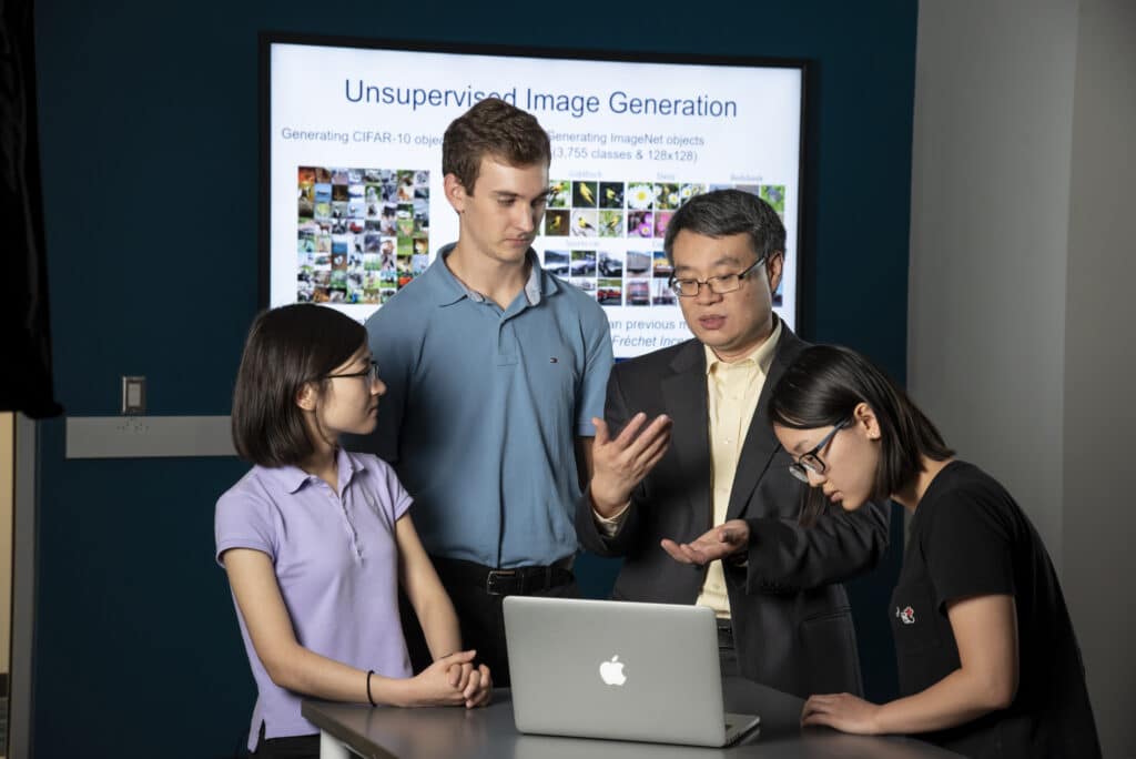 four people discuss while looking at a laptop computer