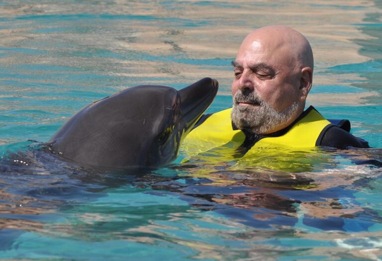 A man in a yellow life vest floating with a dolphin in water