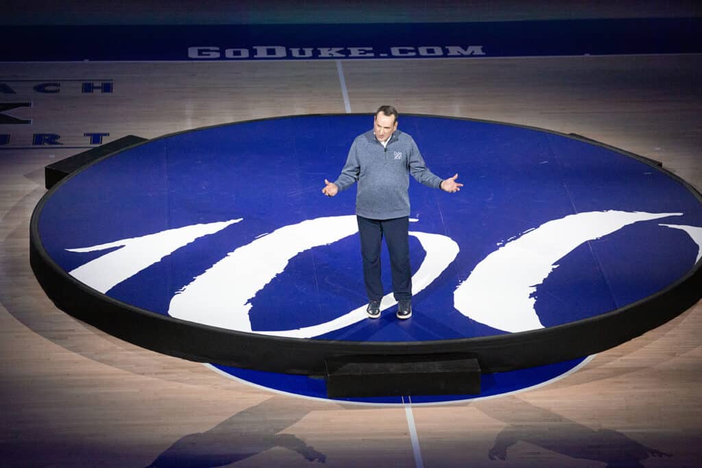 A man stands in the middle of a basketball court lit by a spotlight.