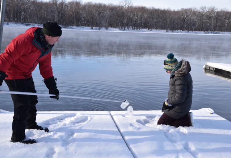 two people in heavy coats in snow at a lakeshore