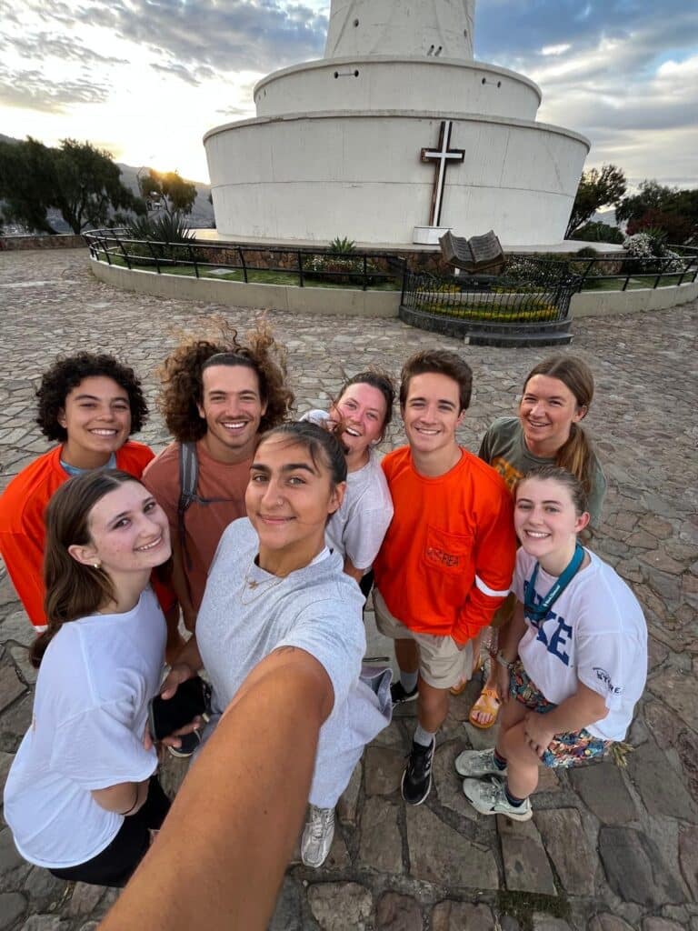 group of students taking a selfie in front of a large structure with a cross on it