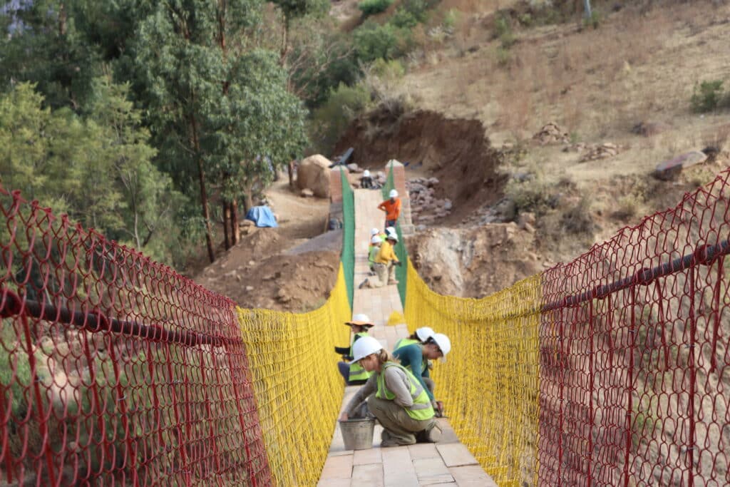 several small groups bent down working on a stable but not complete bridge