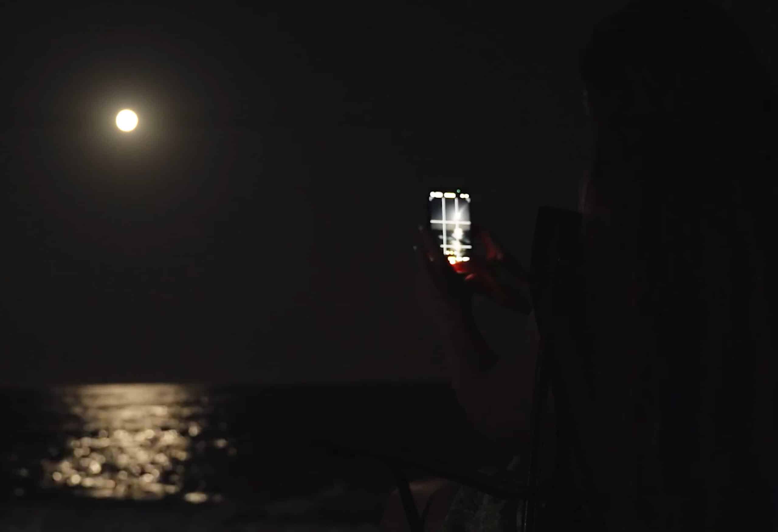 a smart phone takes a photo of the moon over the ocean at night