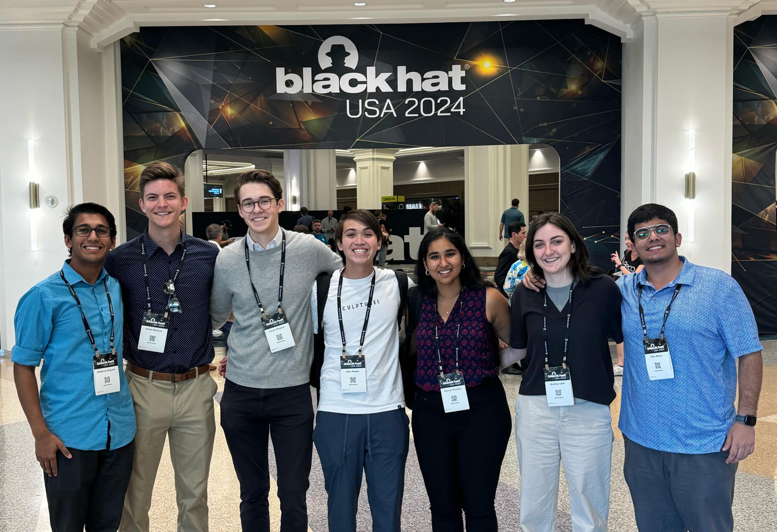 Seven students stand in front of a sign for Black Hat USA 2024