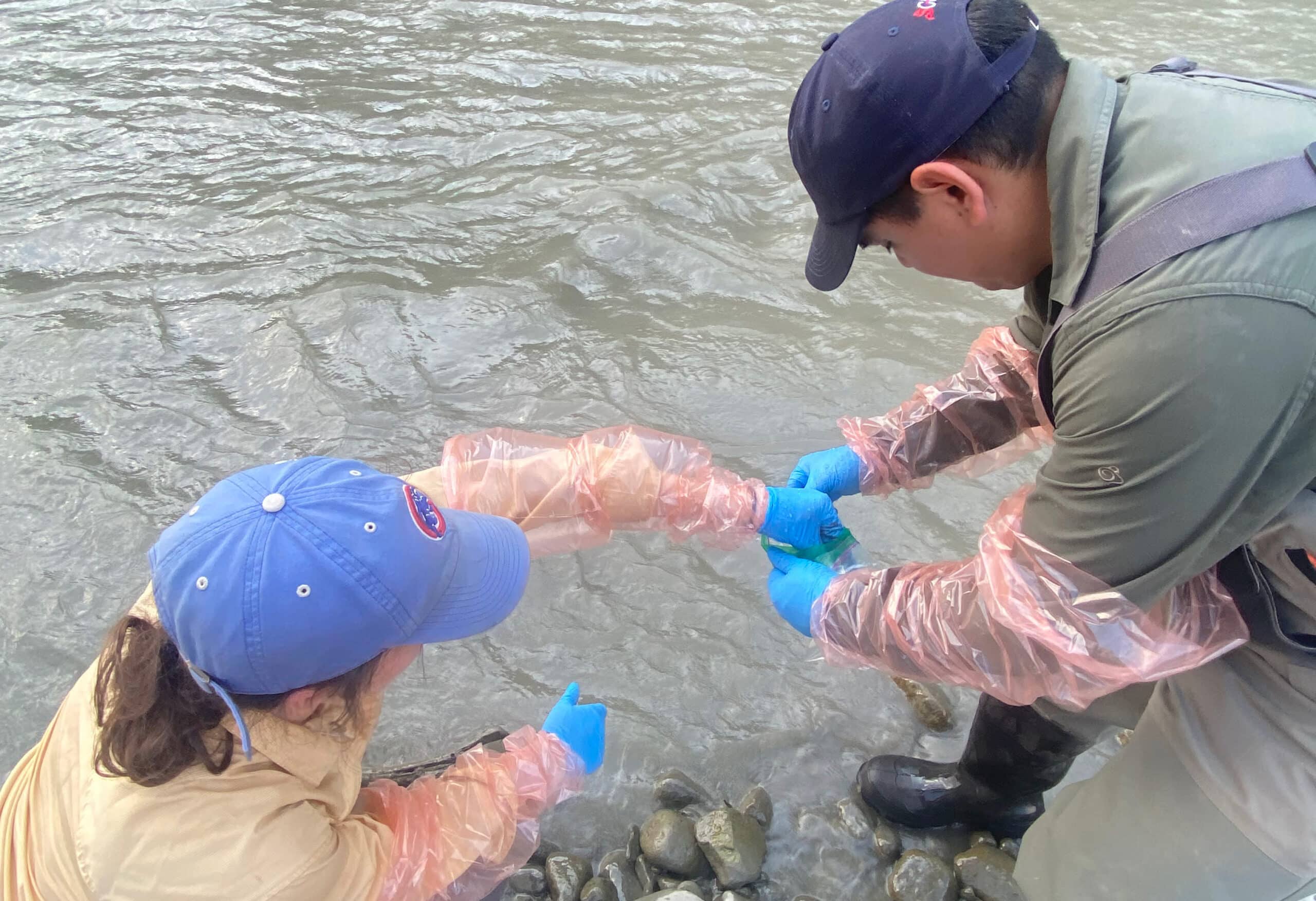 two phd students take water samples in a river