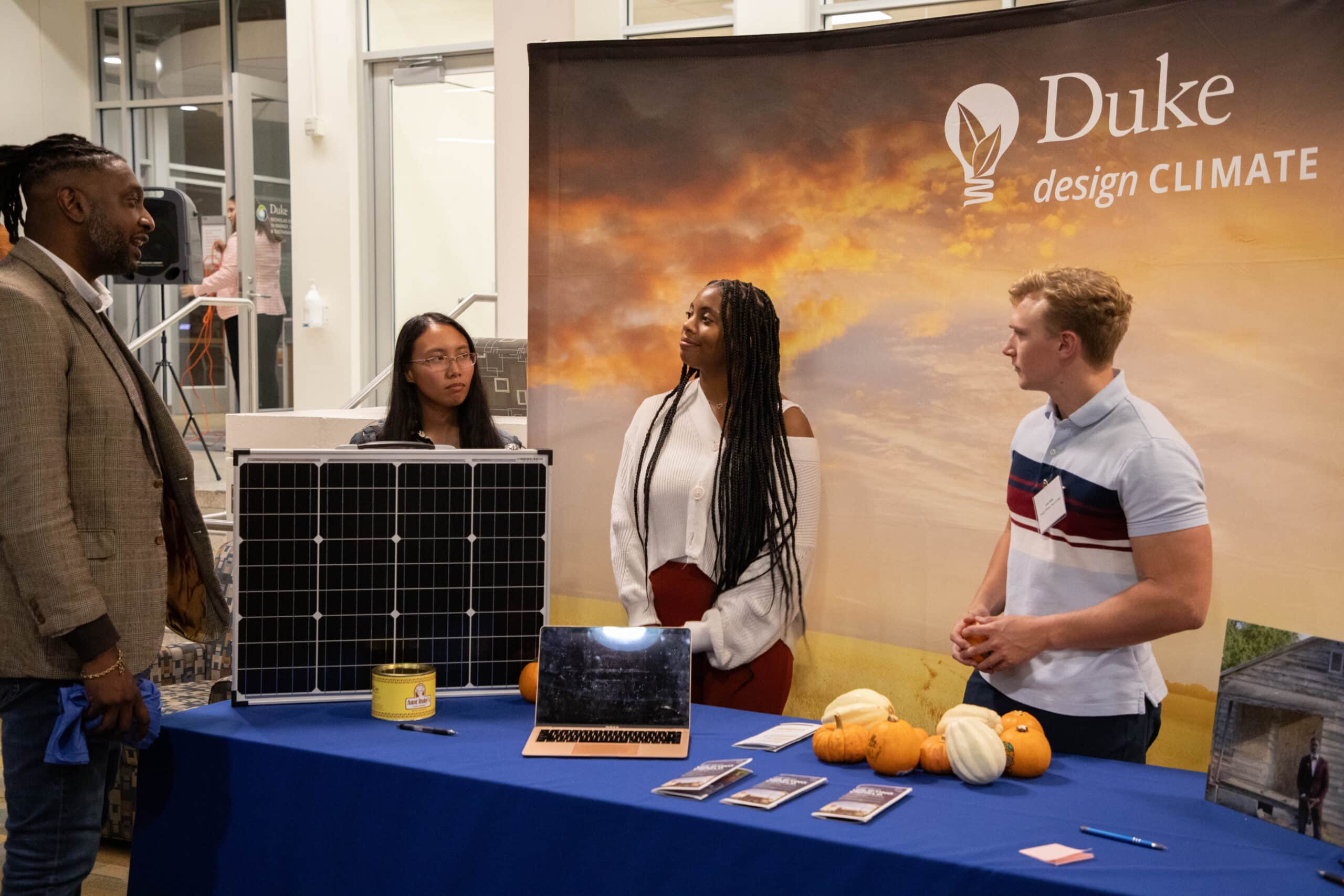 four people discuss around a table with a solar panel and small gourds