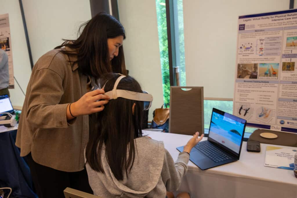 a person stands next to a seated person wearing a VR headset