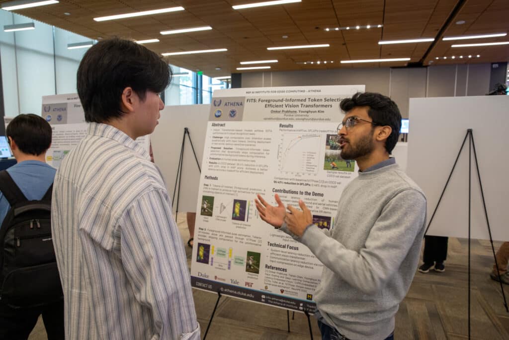 a person speaks in front of a research poster while another person listens