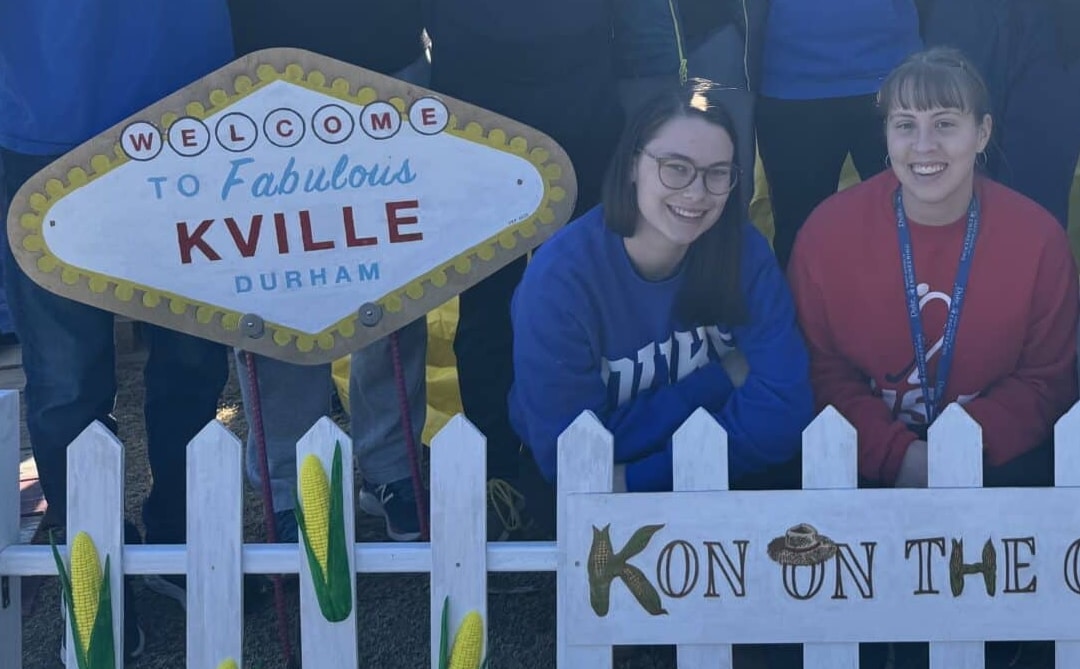 two people kneel next to a handmade sign