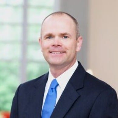 Pat Gunsch smiles in a blue tie and black suit jacket.