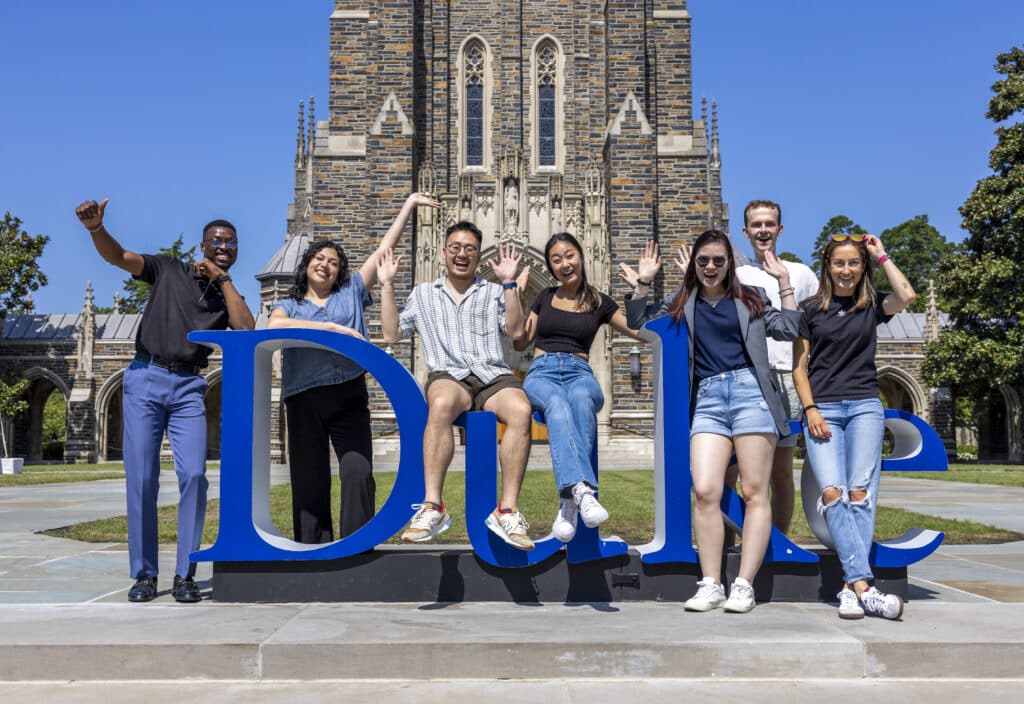 students sitting and standing on large DUKE sign in front of chapel