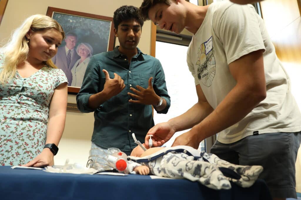 A college student administering CPR to a baby manikin lying on a table.