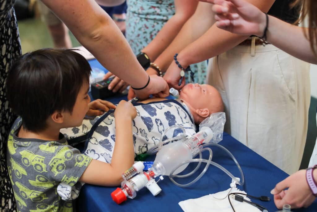A small child touching a baby manikin that is lying on a table.