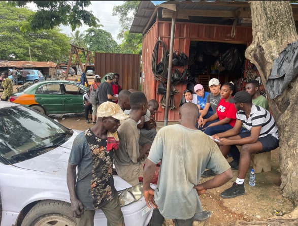 Participants seated on a bench speaking with community members seated on a car in a local village