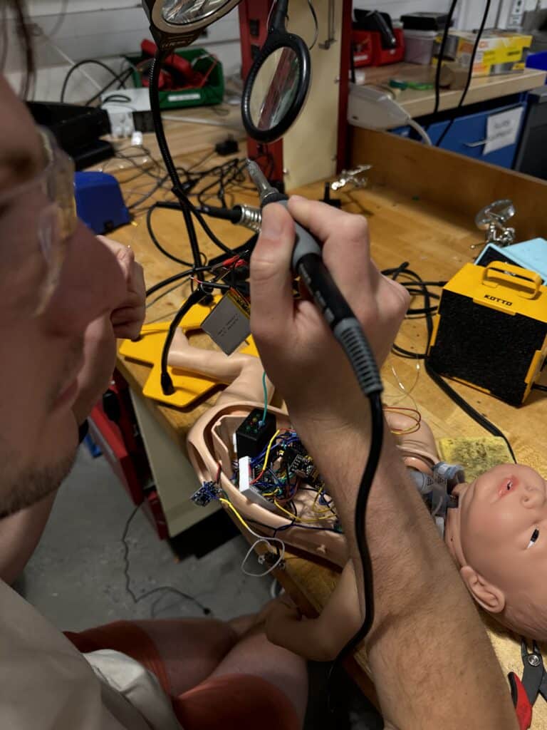 Student with safety glasses soldering wires inside the open chest cavity of a manikin baby.